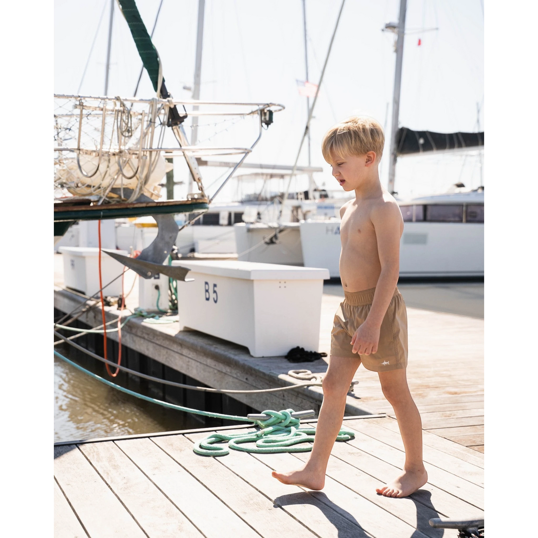 Young boy standing on a dock by a sailboat