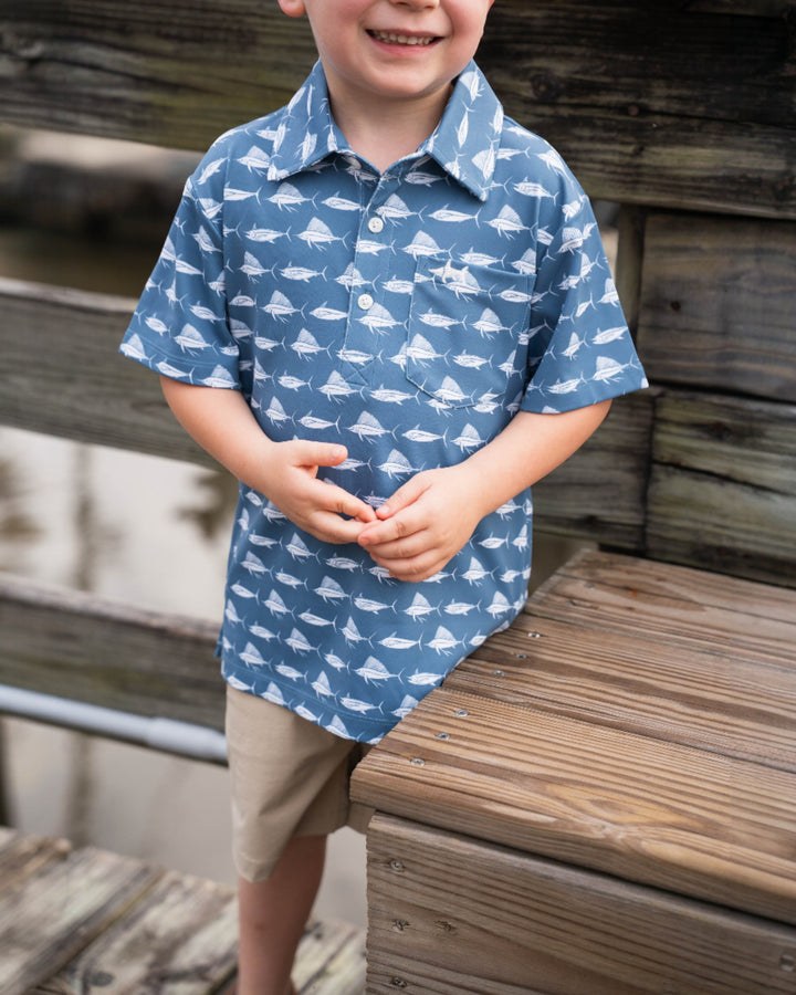 Child wearing a blue shirt with white patterns, standing on a wooden dock.
