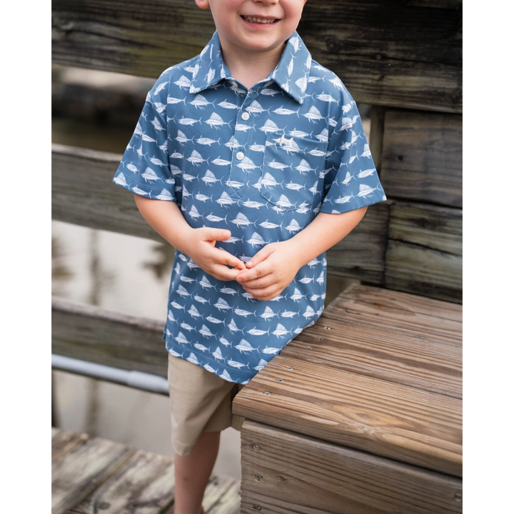 Child wearing a blue shirt with white patterns, standing on a wooden dock.