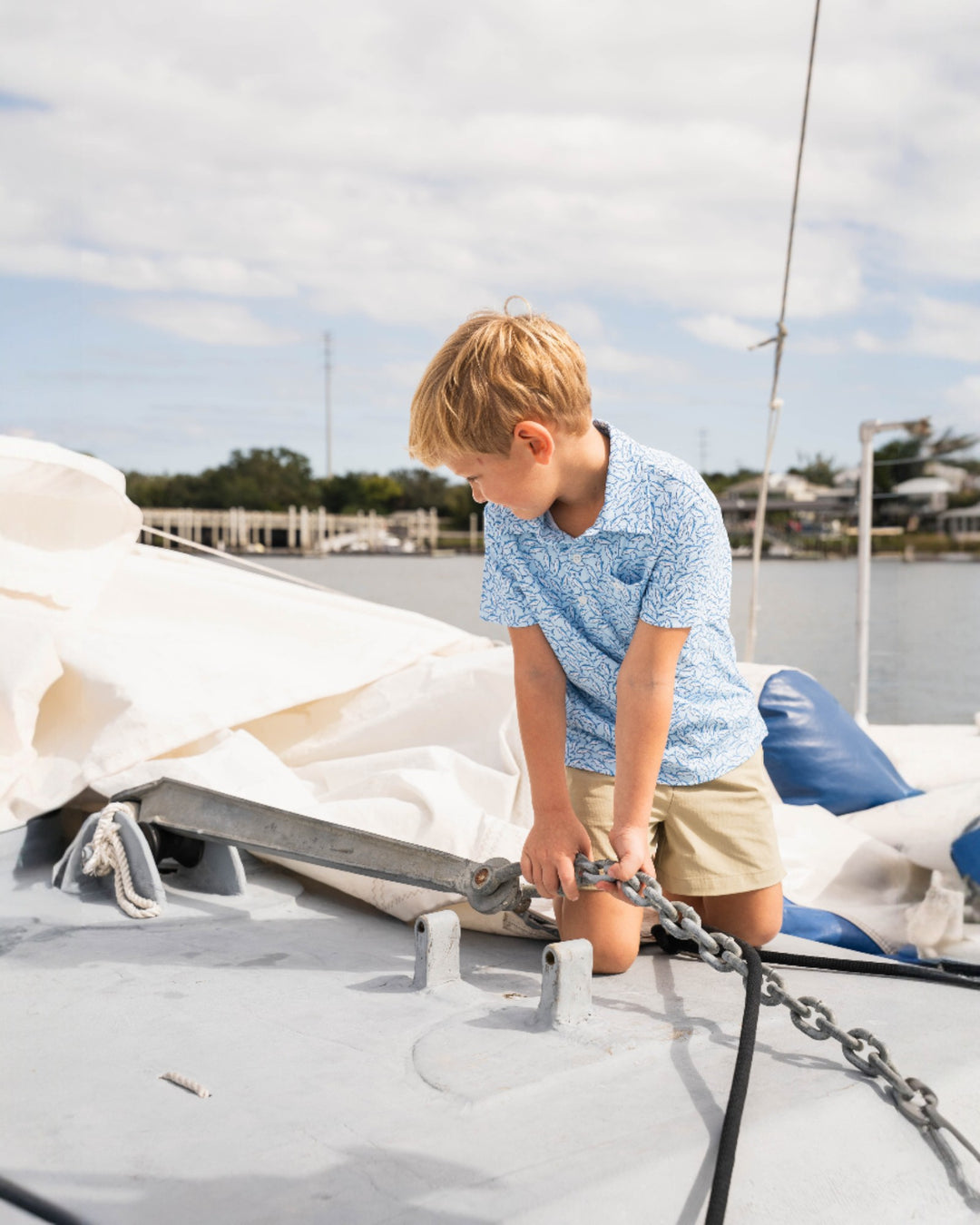Young boy on a sailboat tying a rope to a cleat with water and sky in the background