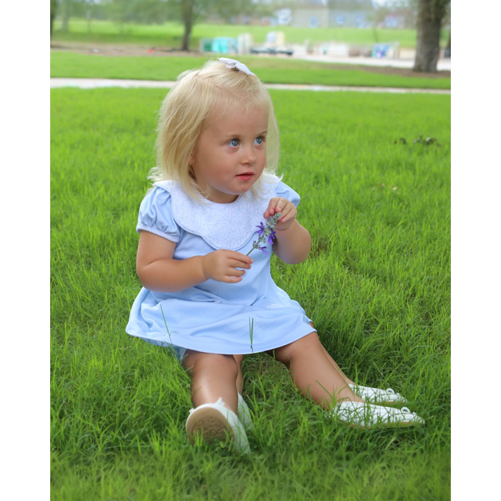 Young girl in a light blue dress sitting on grass holding a flower