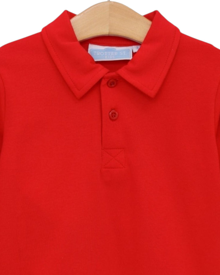 A bright red short-sleeve polo shirt with a collar and two-button placket, shown hanging on a wooden hanger against a plain white background, that store