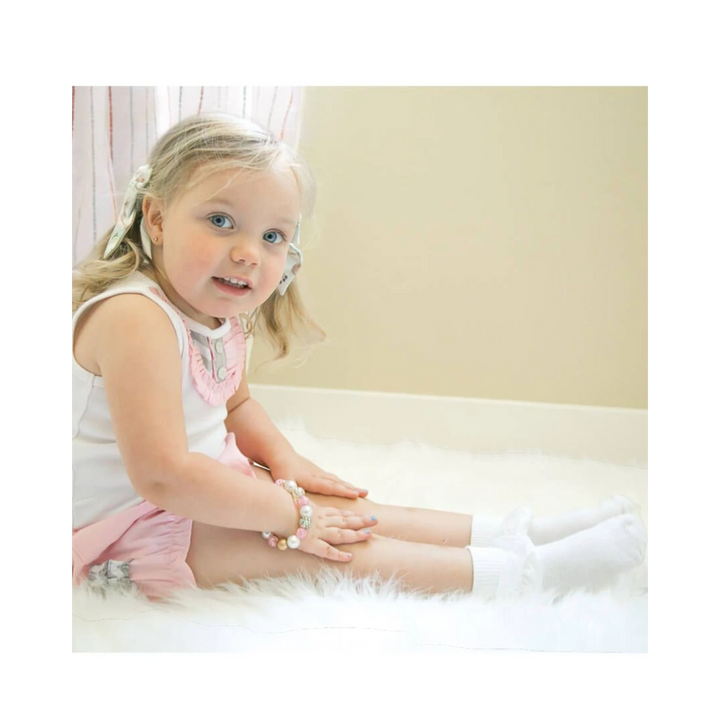 Young girl sitting on a white surface wearing a pink dress and white socks.