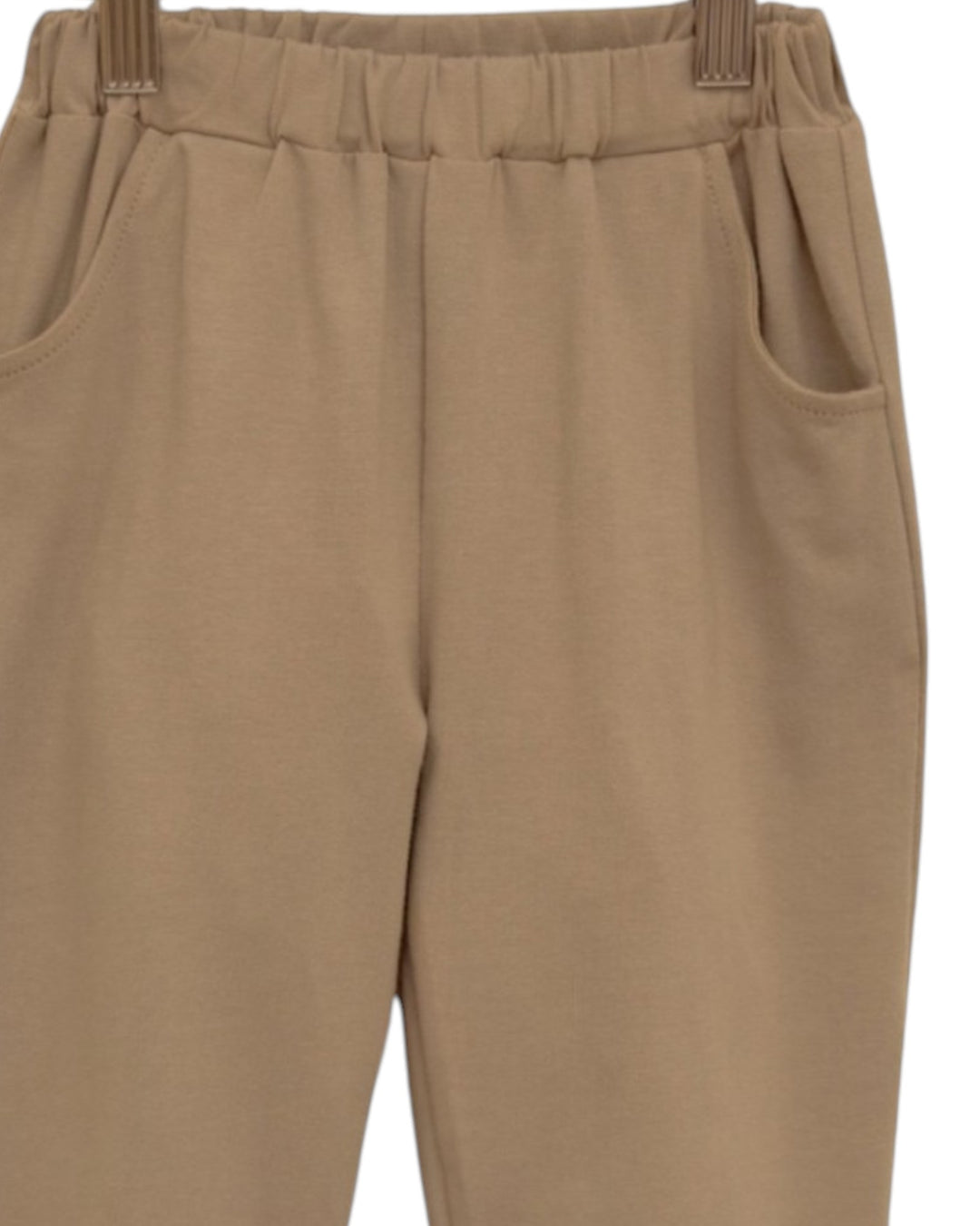 Close-up of beige elastic-waist pants with side pockets, hanging against a plain white background, that store