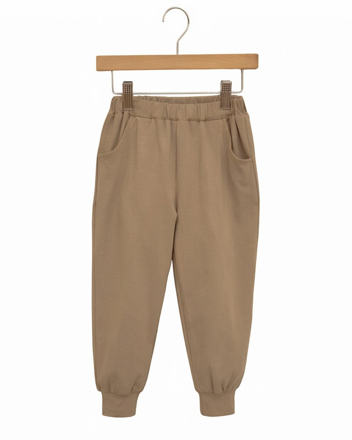A pair of beige jogger pants with an elastic waistband, side pockets, and ribbed cuffs, hanging from a wooden hanger against a plain white background, that store