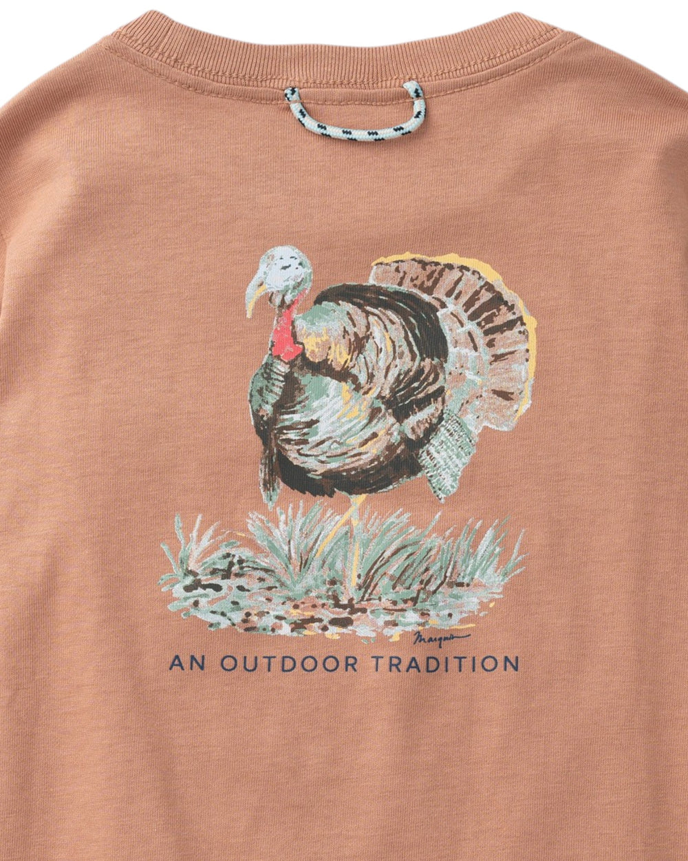 A close-up of a terracotta-colored t-shirt featuring a graphic of a wild turkey standing in grass, with the text 'AN OUTDOOR TRADITION' printed below. A matching neck loop is attached at the collar, that store