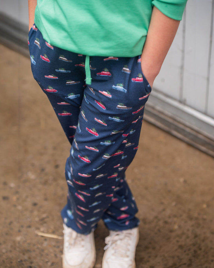 Child wearing navy blue pants with colorful patterns and a green top, standing on a concrete floor.