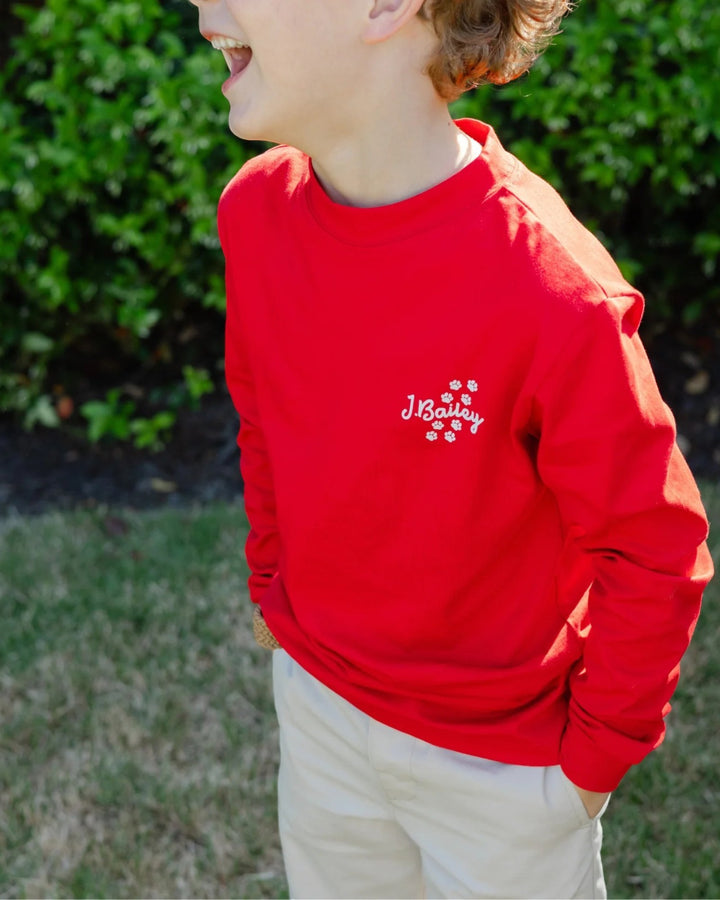 A child wearing a bright red long-sleeve crewneck sweatshirt with a white embroidered &