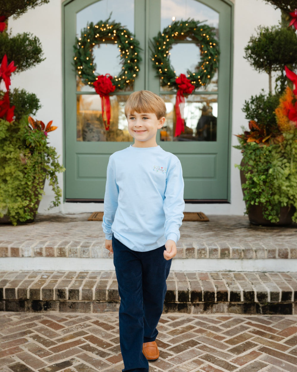 Young boy standing in front of a door with Christmas wreaths and decorations.