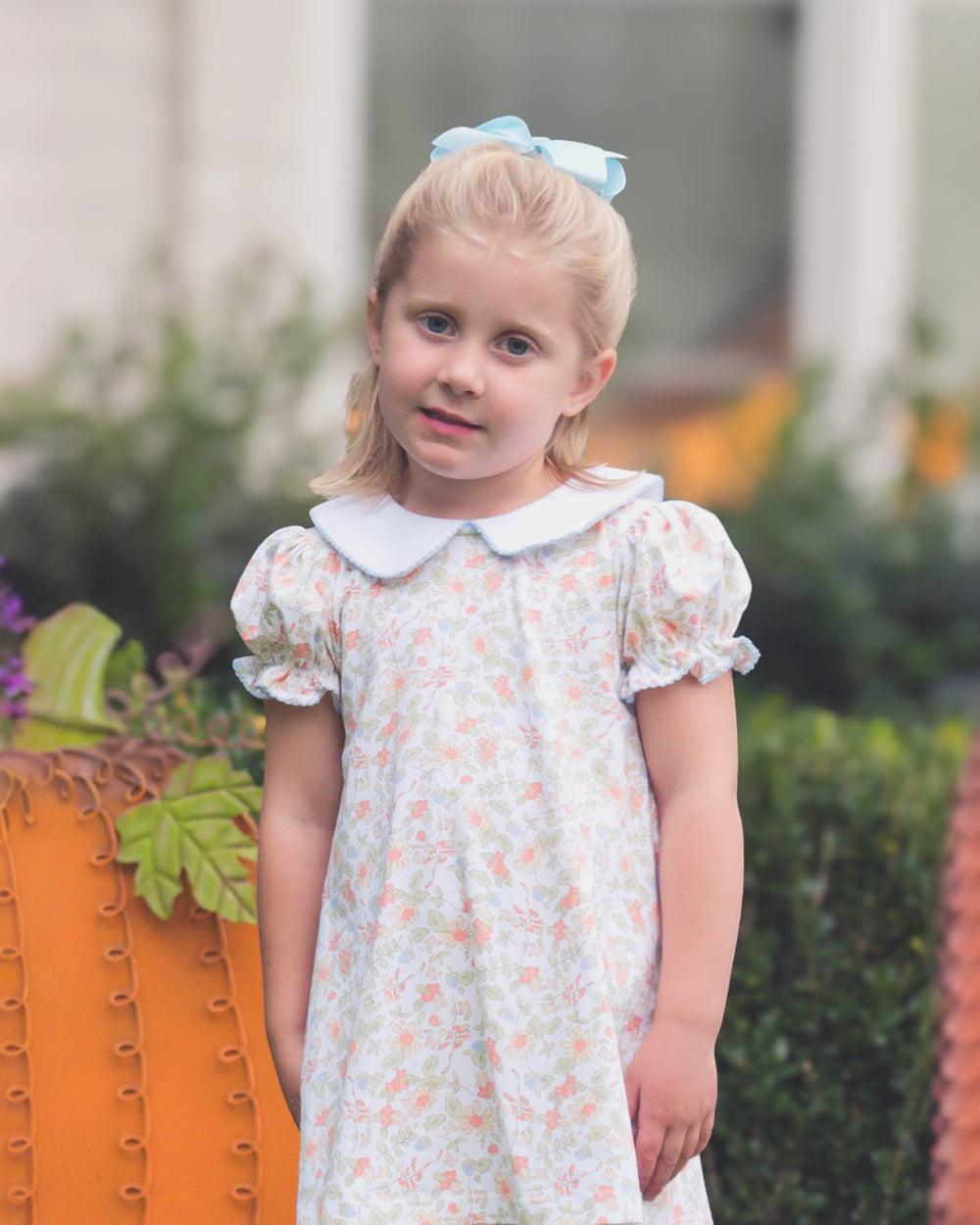 Young girl in a floral dress standing outdoors with blurred background