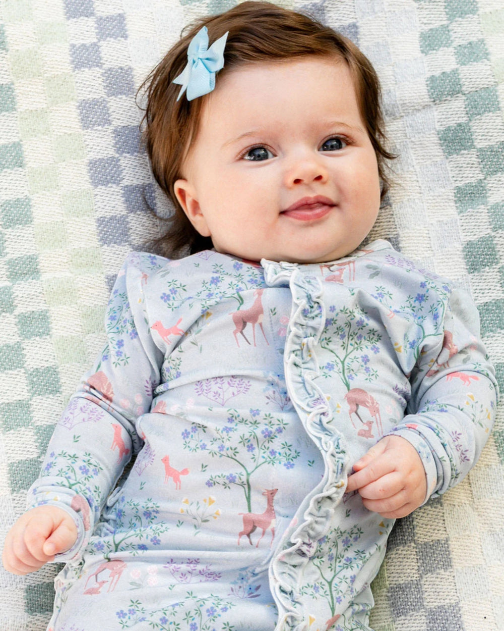 Baby wearing a floral outfit lying on a checkered blanket
