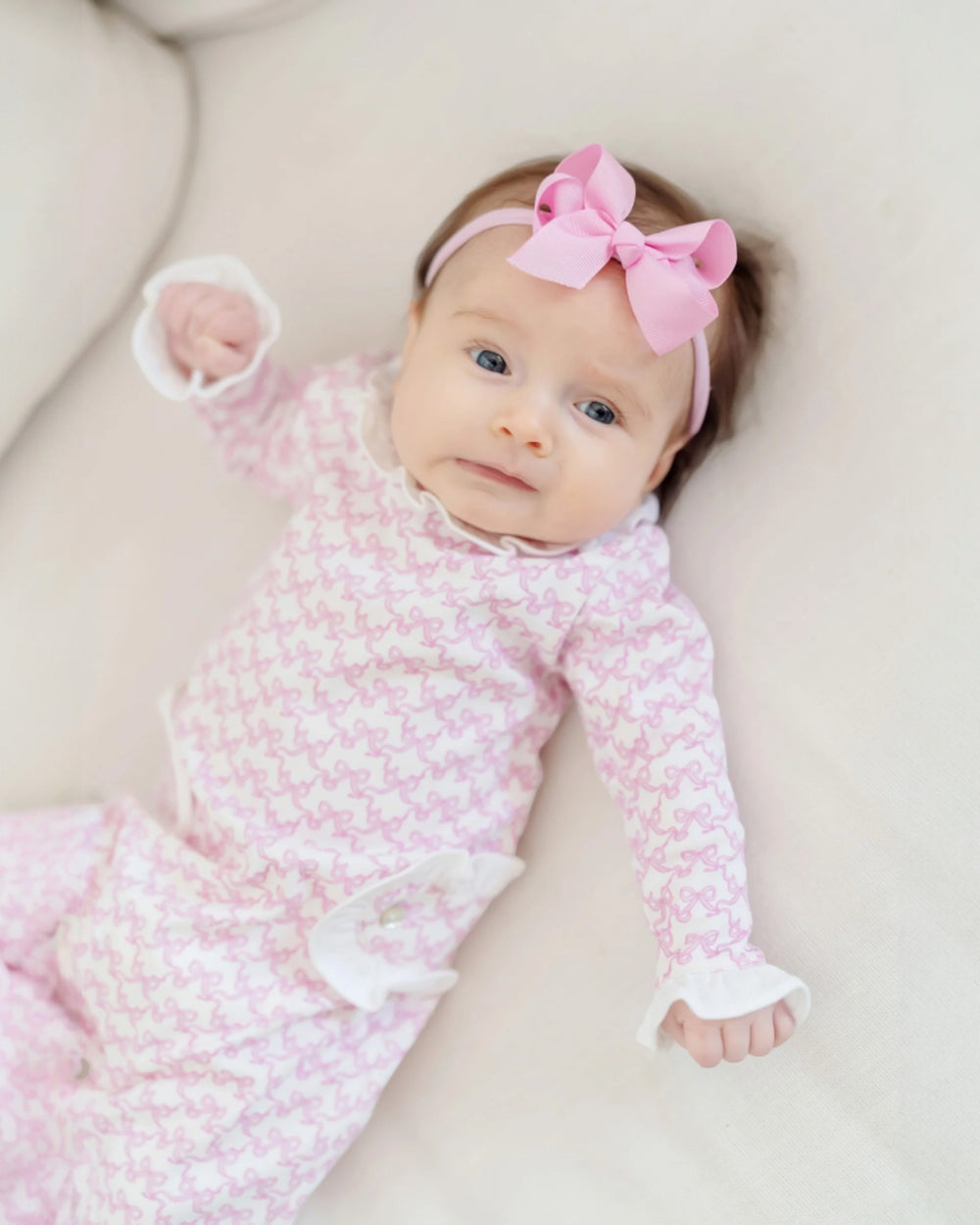 Newborn baby in a pink outfit with a matching headband on a light background