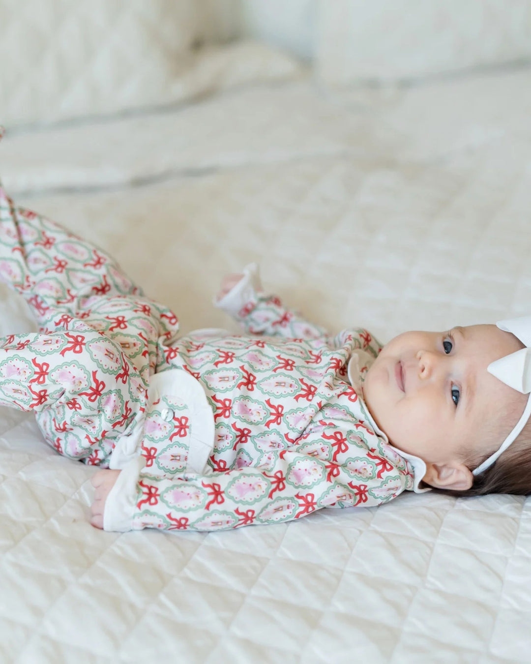 Baby lying on a bed wearing a patterned outfit with red bows.