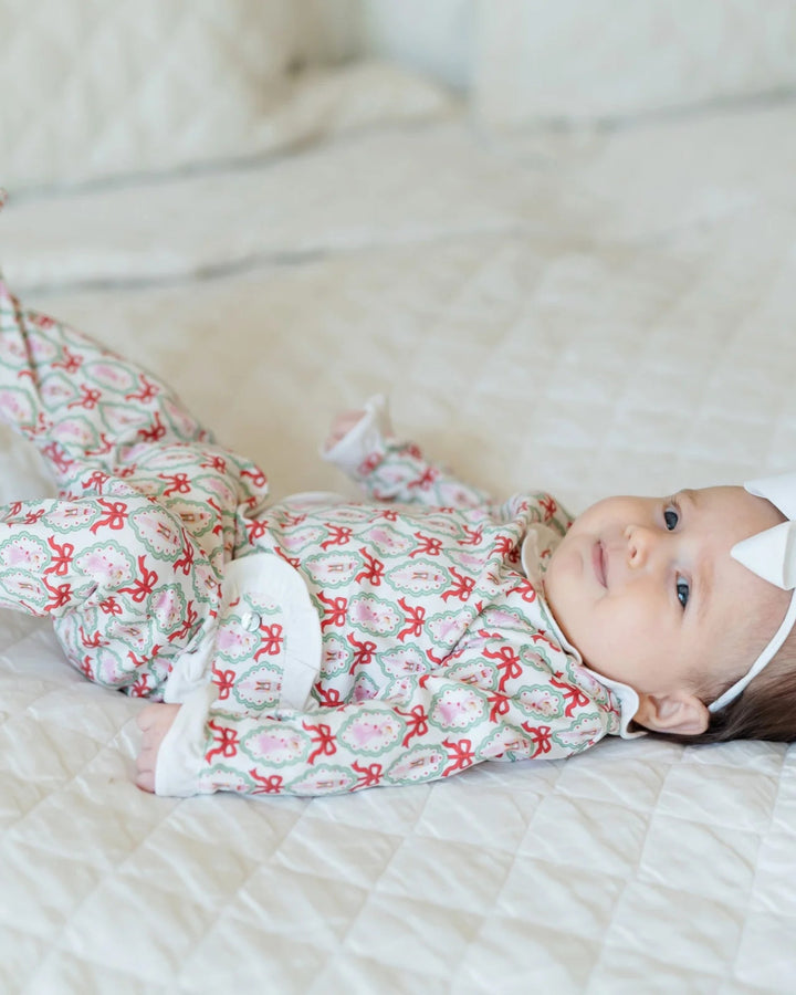 Baby lying on a bed wearing a patterned outfit with red bows.