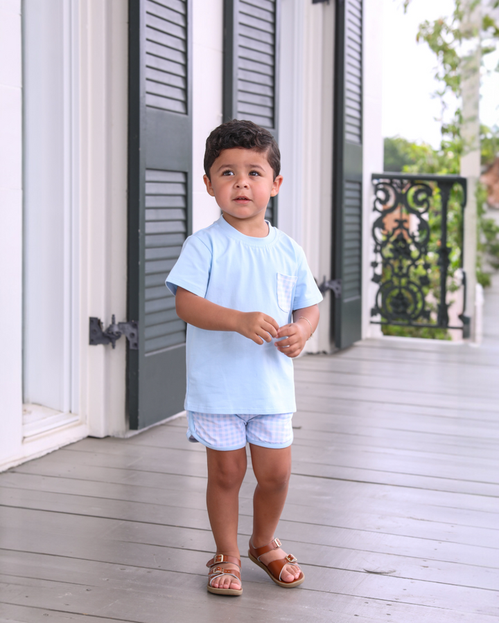 Child wearing a light blue outfit standing on a wooden deck.