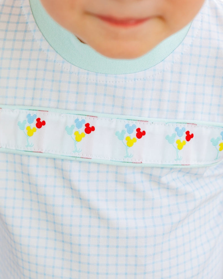 Close-up of a baby wearing a white bib with a light blue gingham pattern, a mint green collar, and a decorative horizontal band featuring colorful balloon motifs, that store