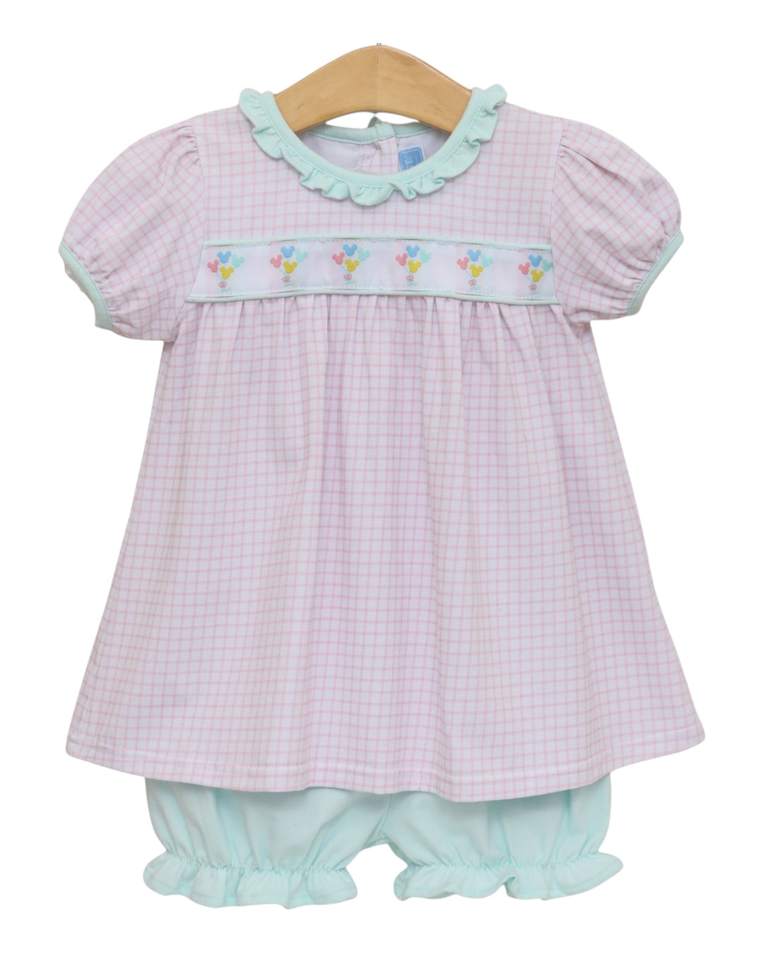 A baby girl's two-piece outfit featuring a short-sleeve smocked dress in a light pink and white gingham pattern with mint green ruffle trim and a floral smocked chest band, paired with matching mint green ruffled bloomers, hanging on a wooden hanger against a white background, that store