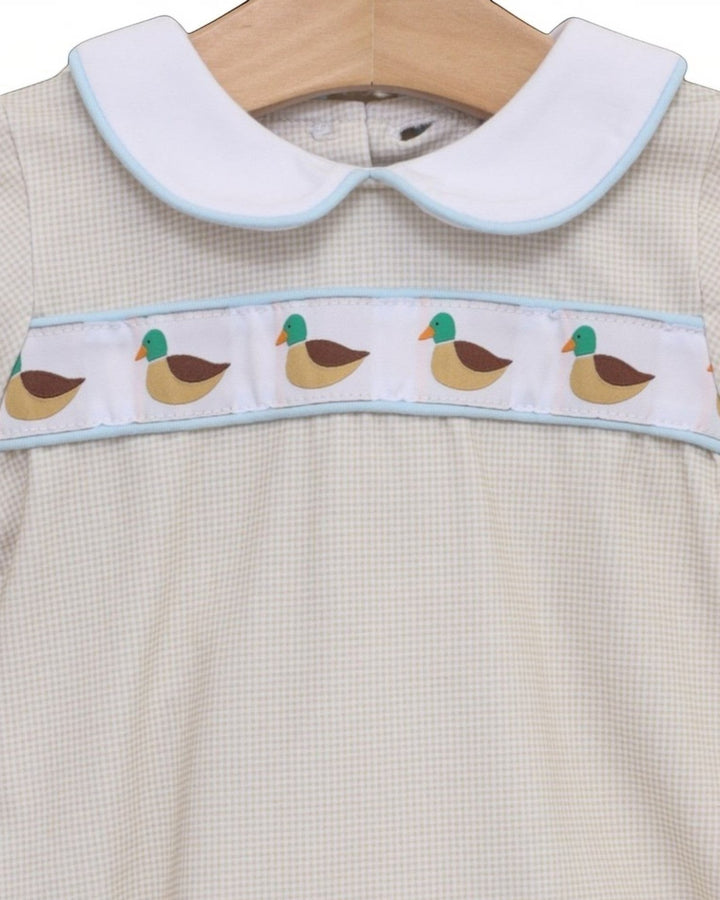 A close-up of a baby dress featuring a white Peter Pan collar with light blue trim, a white chest band decorated with a repeating duck pattern, and a cream-colored gingham fabric body, that store