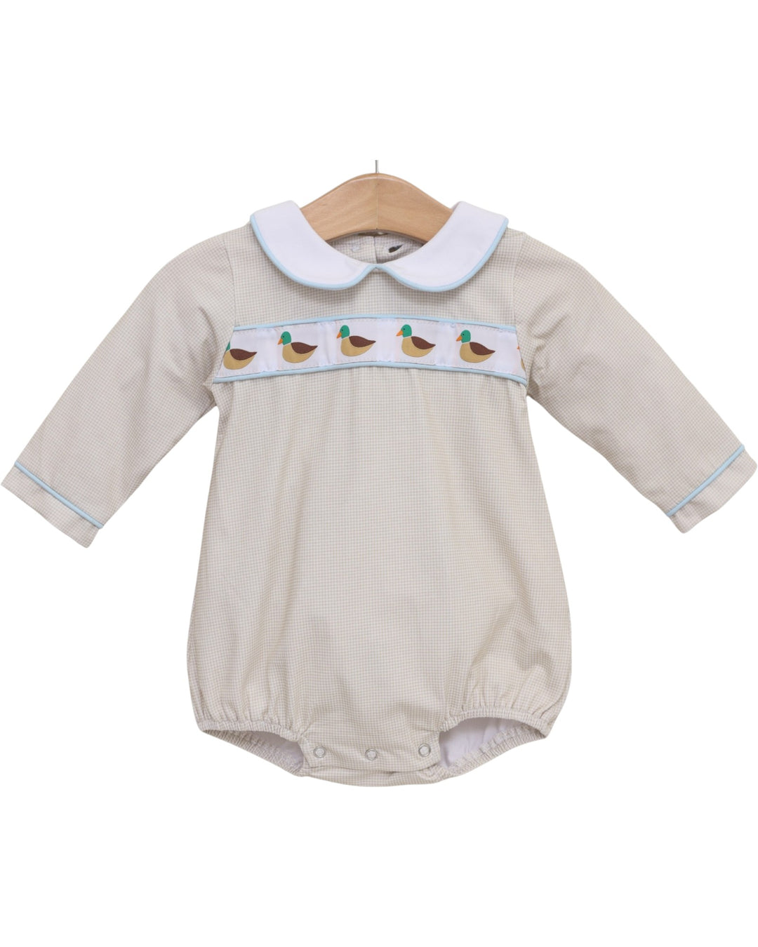 A baby long-sleeve romper in beige with a white Peter Pan collar, featuring a smocked chest band with embroidered ducks and light blue piping, hanging on a wooden hanger against a white background, that store