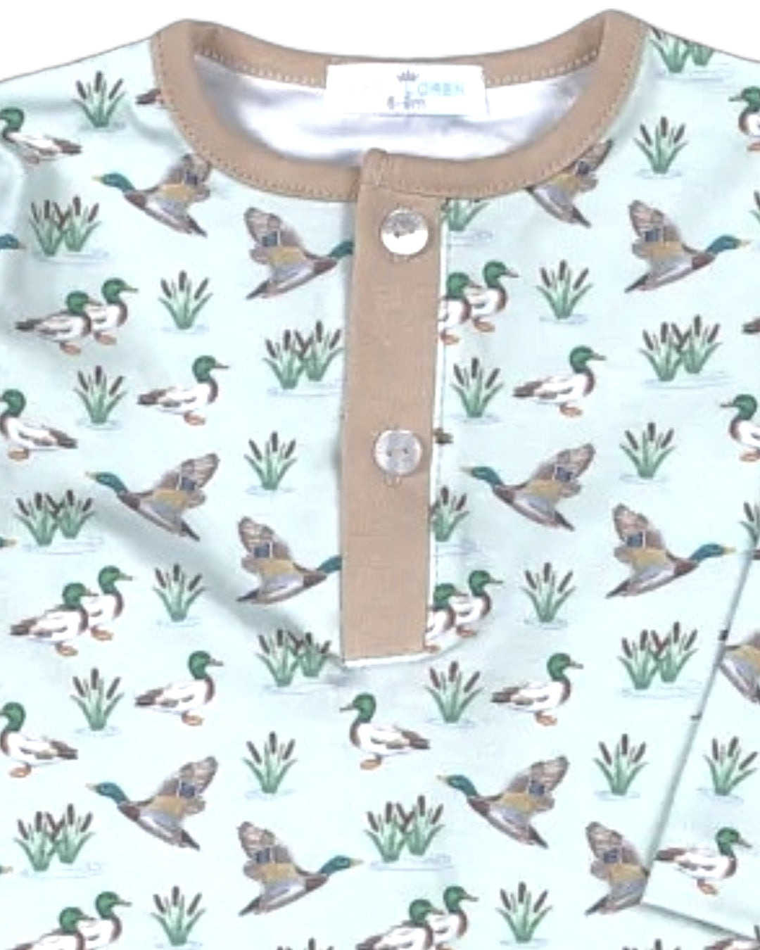 A close-up of a baby Henley shirt featuring a repeating pattern of mallards and reeds on a pale mint green background, with a tan collar and placket, that store