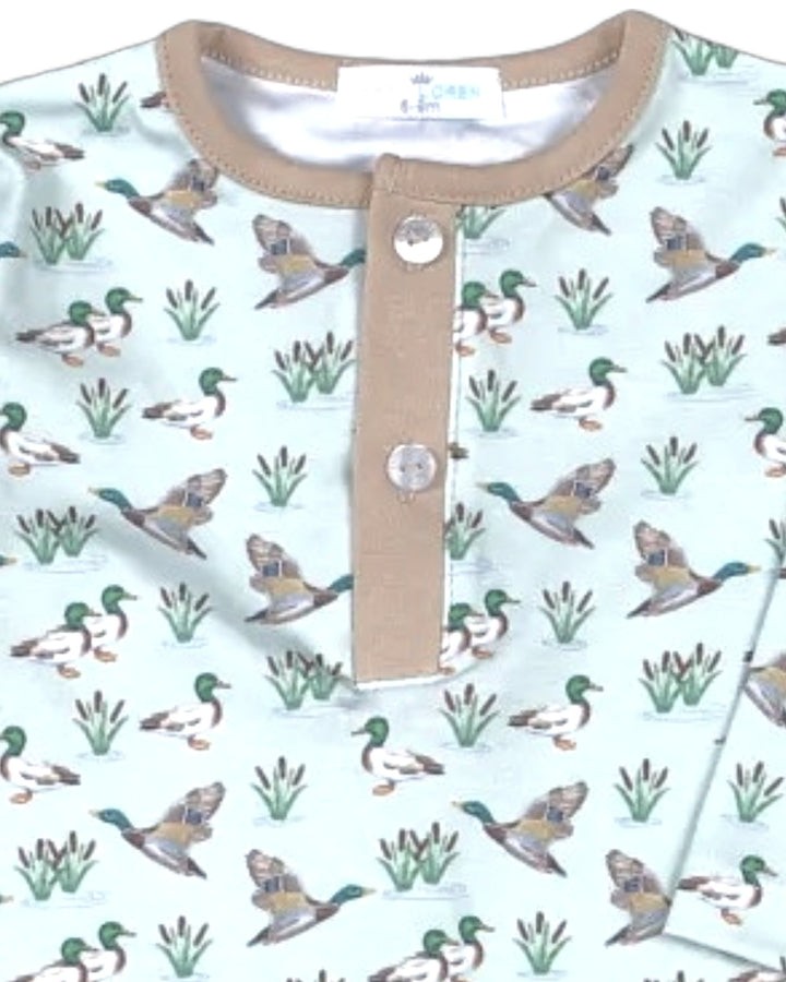 A close-up of a baby Henley shirt featuring a repeating pattern of mallards and reeds on a pale mint green background, with a tan collar and placket, that store