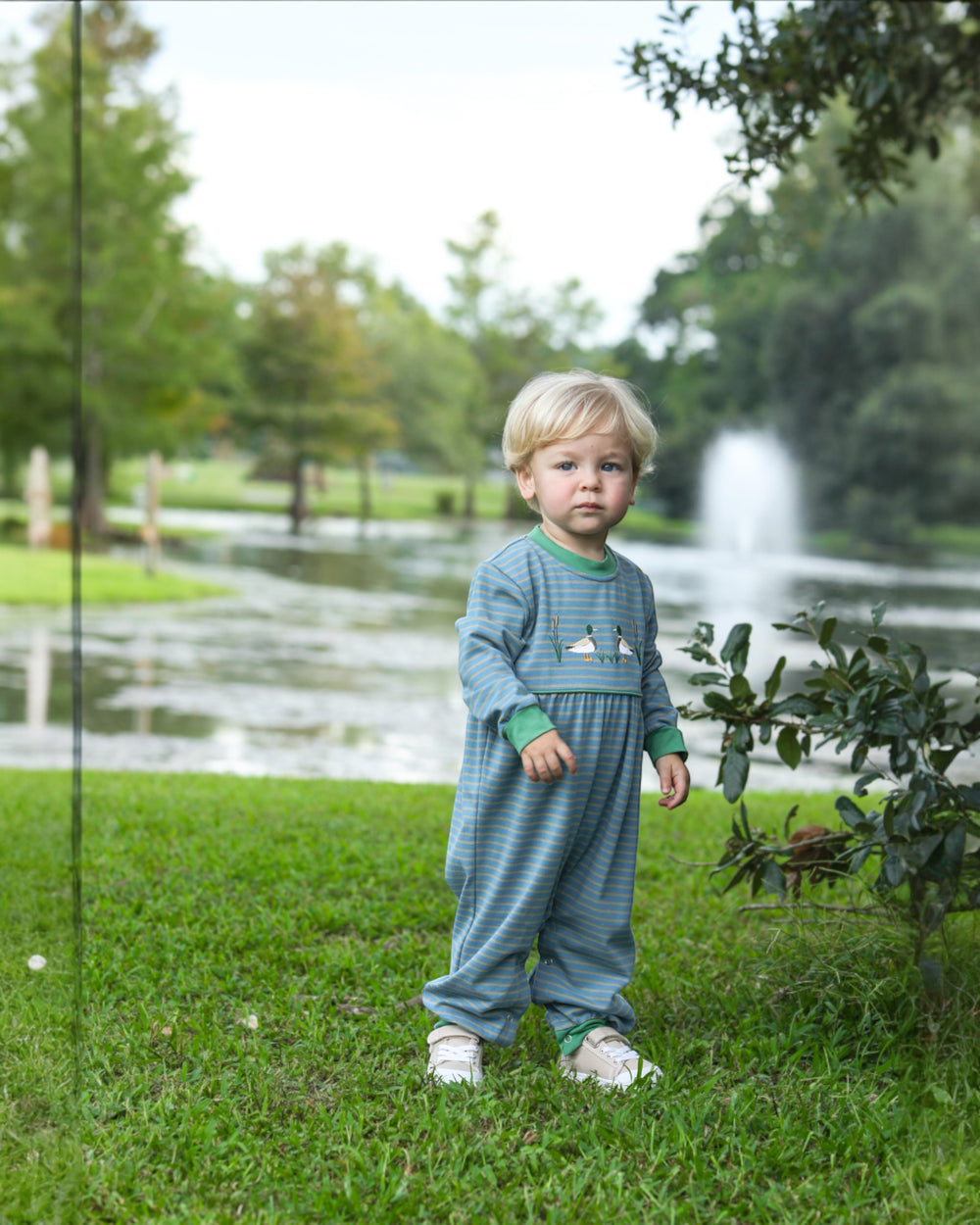 Child in a blue outfit standing in a park with trees and a fountain in the background