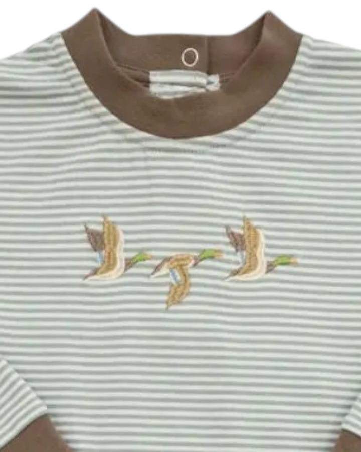 A close-up of a striped baby t-shirt with a brown ribbed crew neck and sleeve cuffs. The shirt features thin horizontal stripes in light gray and white, with a central embroidered motif of three flying ducks in beige and brown tones with small green accents, that store