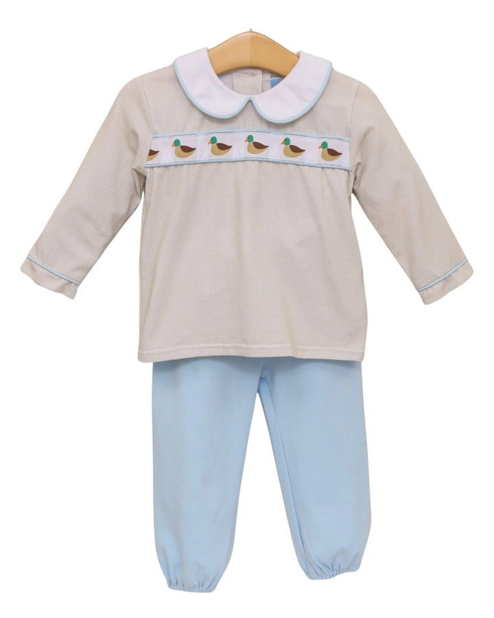 A baby two-piece outfit set consisting of a long-sleeve smocked top in beige with a white Peter Pan collar, a horizontal band of embroidered ducks, and light blue pants, shown on a wooden hanger against a white background, that store
