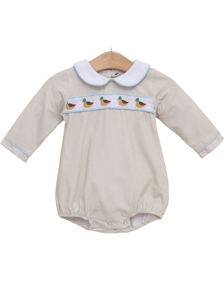 A baby long-sleeve romper in beige with a white Peter Pan collar, featuring a smocked chest band with embroidered ducks and light blue piping, hanging on a wooden hanger against a white background, that store