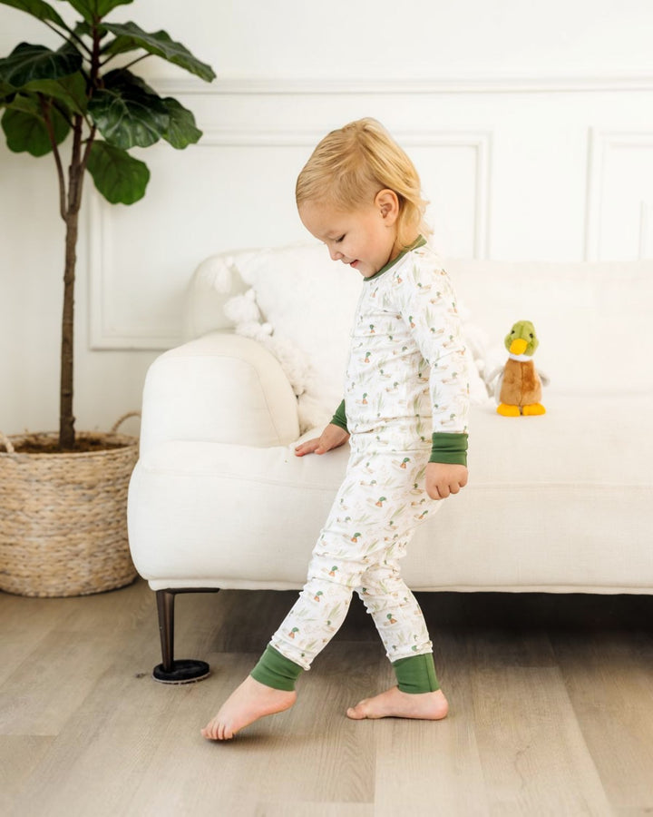 A toddler walking barefoot in a bright room, wearing a white long-sleeve pajama set with a small repeating pattern and green cuffs and collar, that store