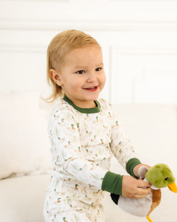 A young child wearing long-sleeve duck-print pajamas holds a plush duck toy in a bright, white indoor setting, that store
