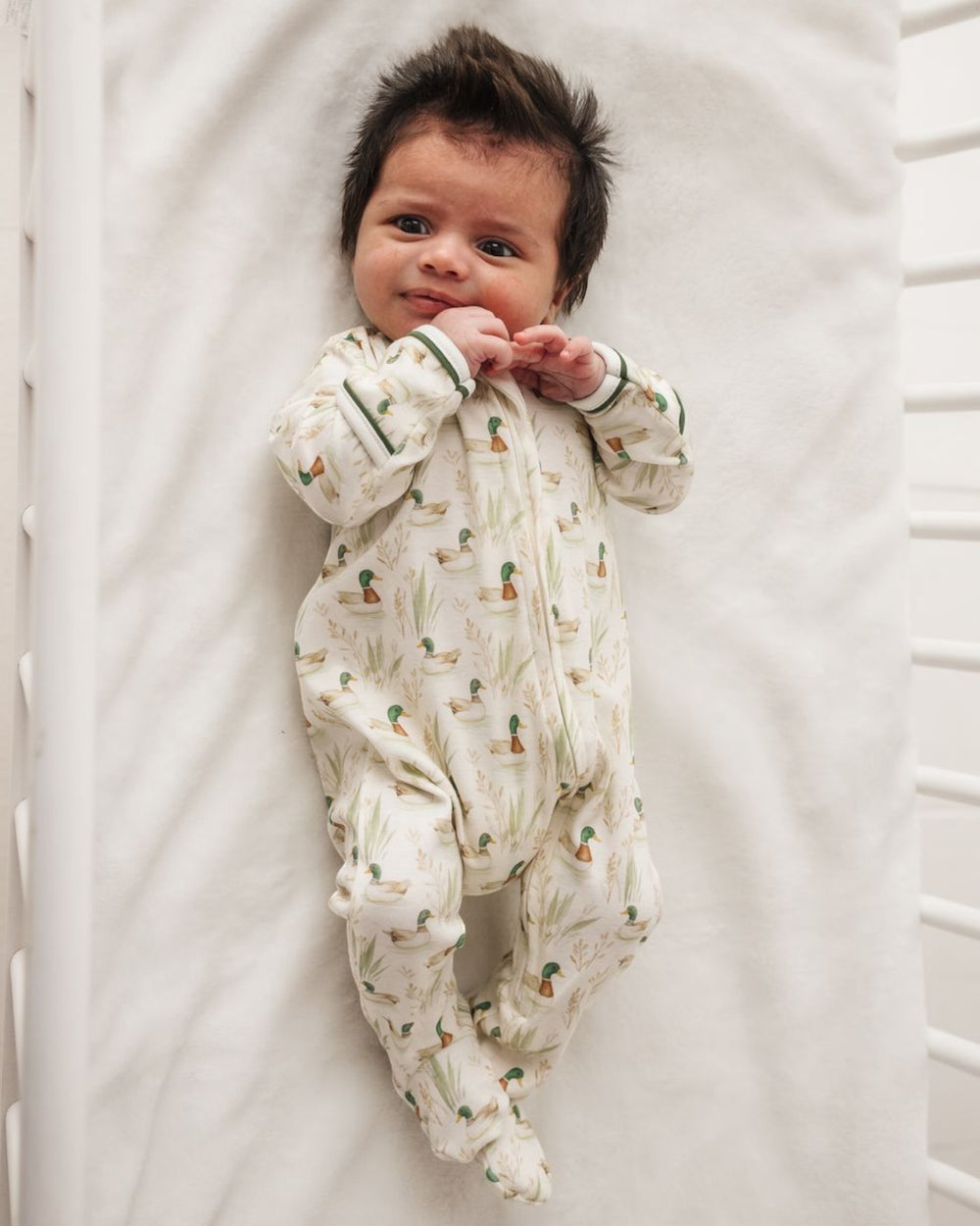 A newborn baby lying on their back on a white mattress, wearing a cream-colored footed sleeper with a green and orange cactus pattern, that store