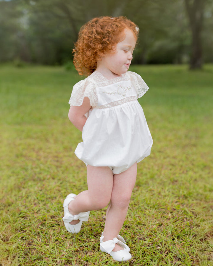 Child in a white dress standing on grass