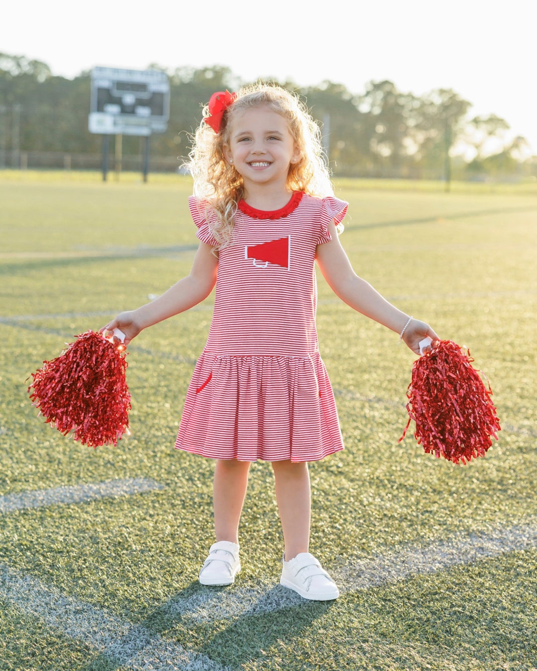 Young girl in a red and white dress with pom-poms on a sports field