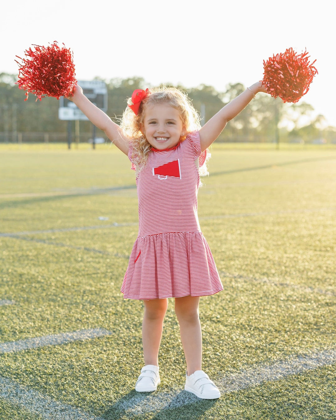 Young girl in a red and white striped dress with pom-poms on a sports field
