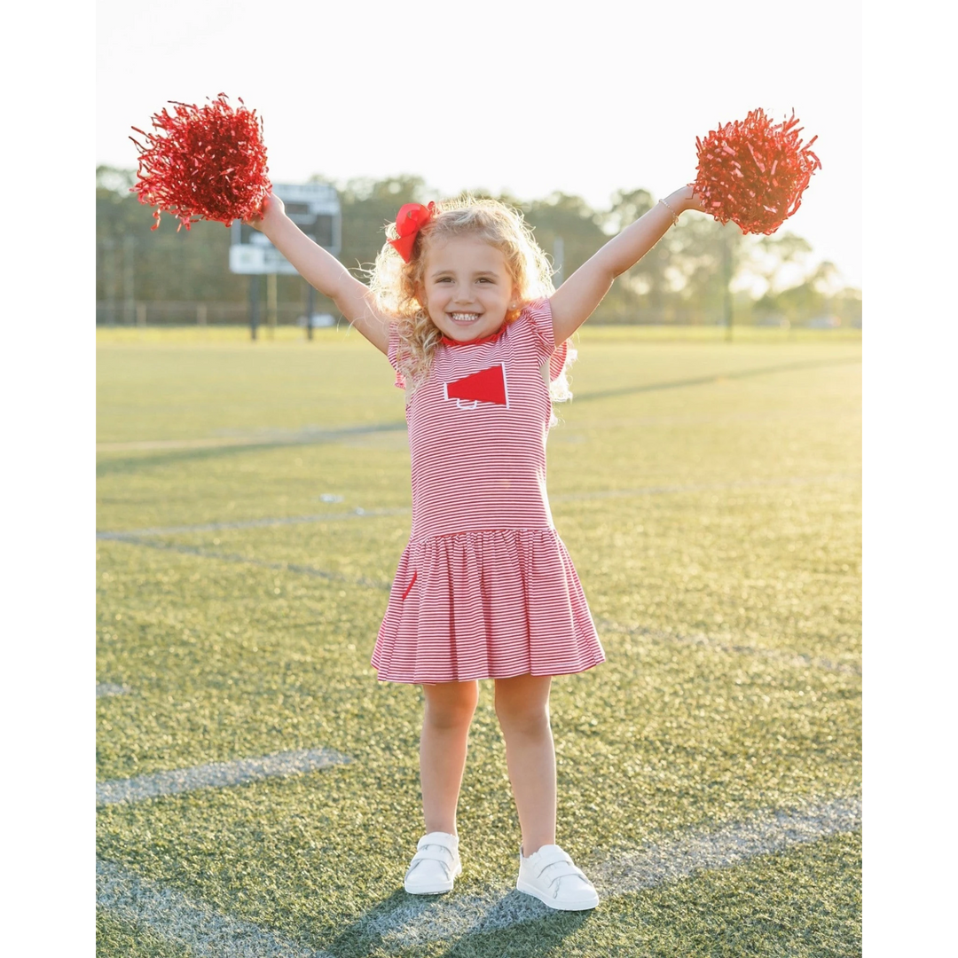 Young girl in a red and white striped dress with pom-poms on a sports field