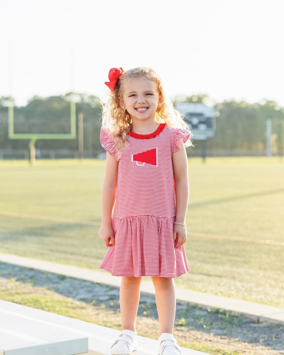 Young girl in a red and white striped dress with a heart design, standing outdoors.