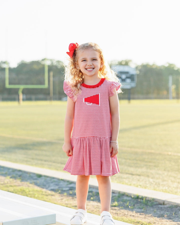 Young girl in a red and white striped dress with a heart design, standing outdoors.