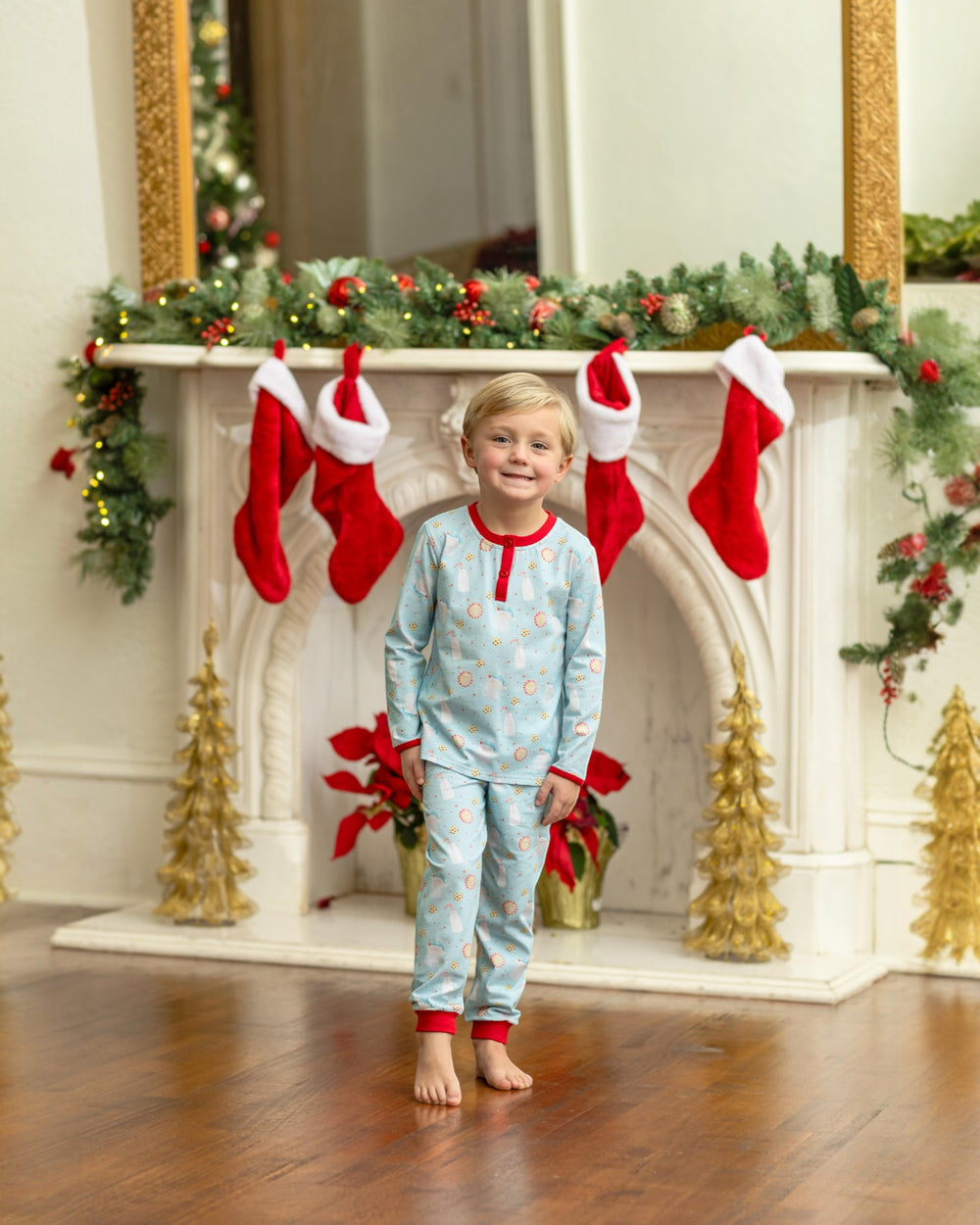 Child in pajamas standing in front of a decorated fireplace with stockings.