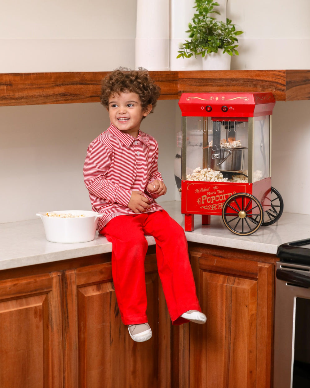Child sitting on a kitchen counter with a red popcorn machine