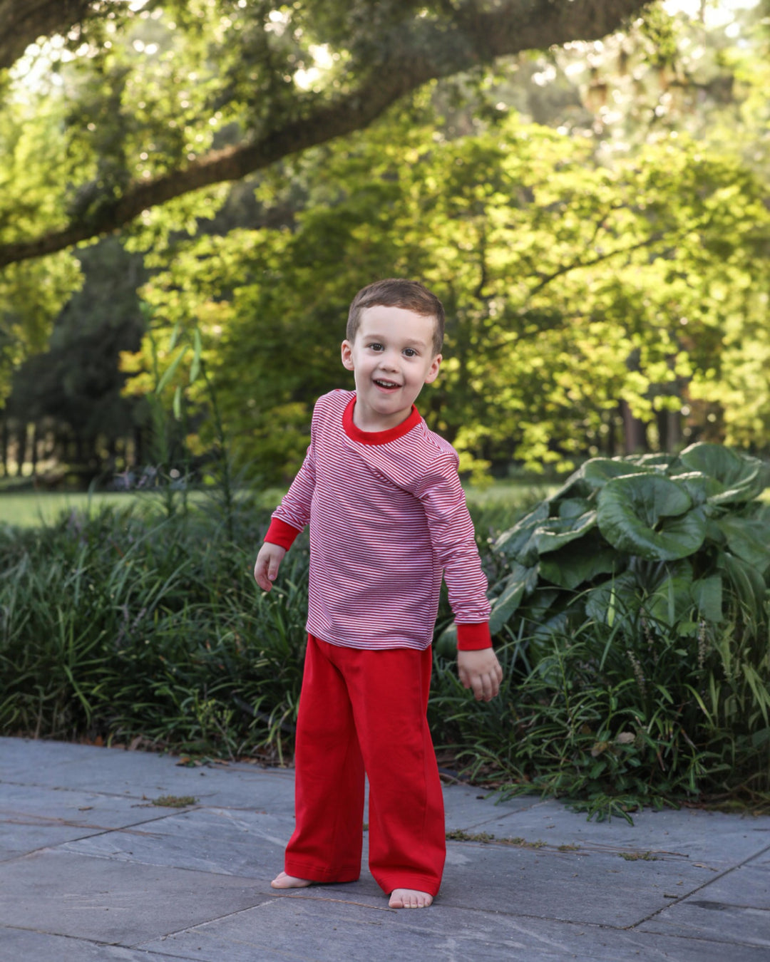Child wearing a pink and red outfit standing outdoors with greenery in the background