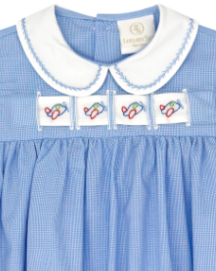 Close-up of a light blue gingham dress with a white Peter Pan collar, blue trim, and four white embroidered patches across the chest, that store