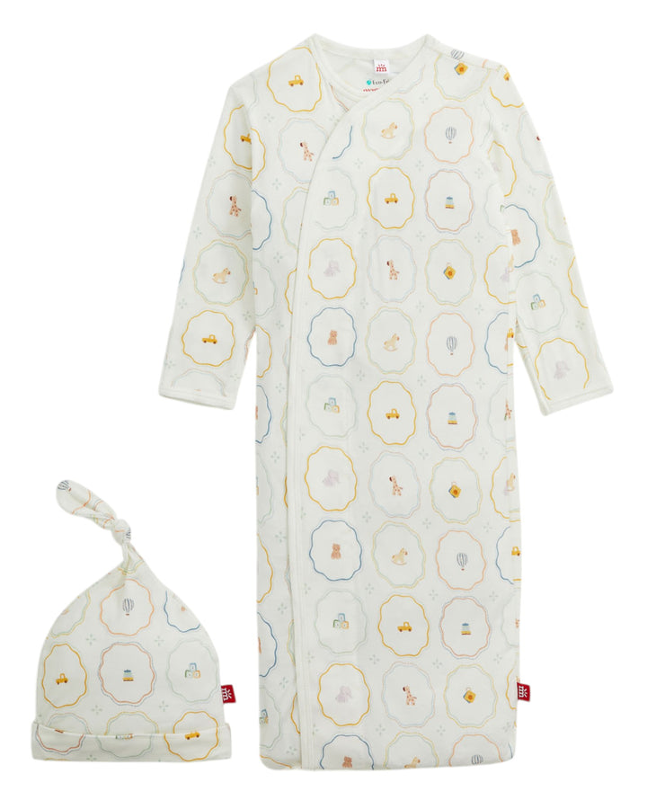 A baby sleep sack and matching knotted beanie set in a warm off-white cotton muslin fabric, both featuring a repeating pattern of scalloped hexagonal circles in yellow, blue, and gray with tiny illustrated characters inside, that store
