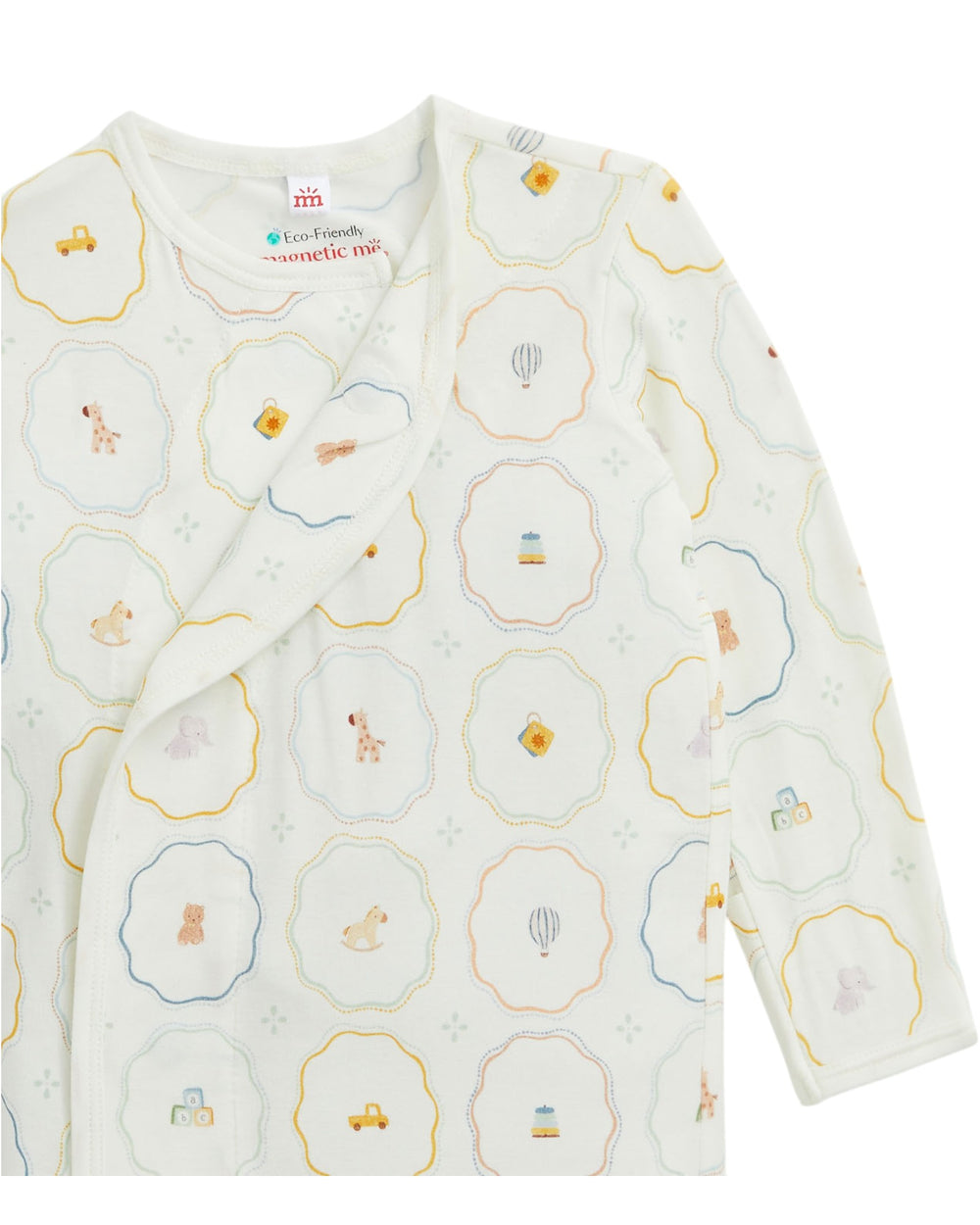A baby long-sleeve wrap sleeper by Eco-Friendly Sleepwear Co. in their 'Magic Tree' pattern, featuring a cream base with a playful print of teddy bears, hot air balloons, and vehicles inside scalloped hexagonal frames outlined in yellow, blue, and orange, that store