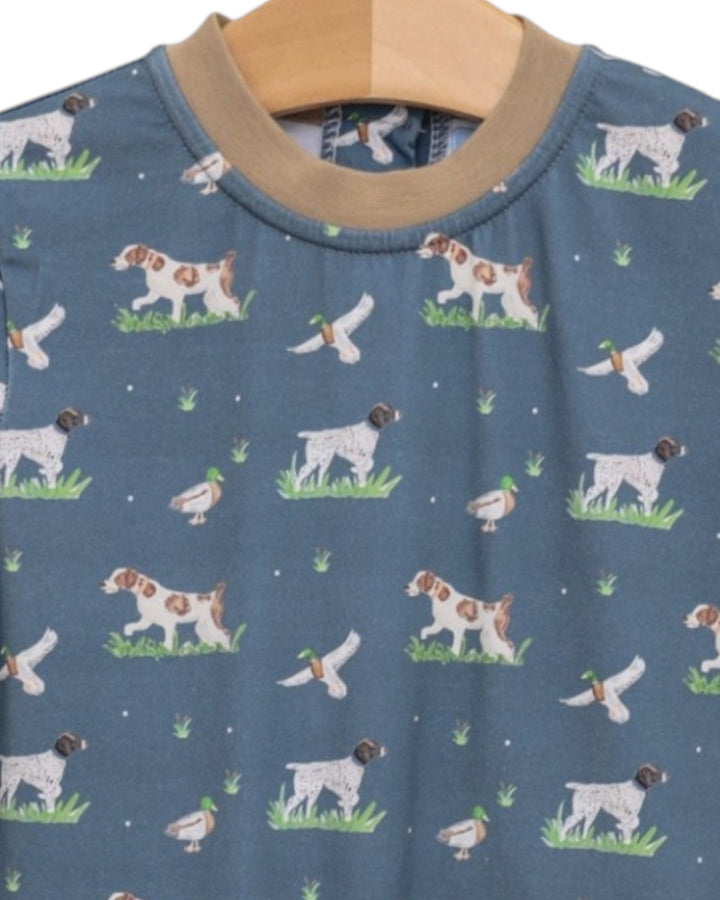 A close-up of a blue long-sleeve shirt with a repeating pattern of hunting dogs, ducks, and ducks with ducklings on a wooden hanger, that store