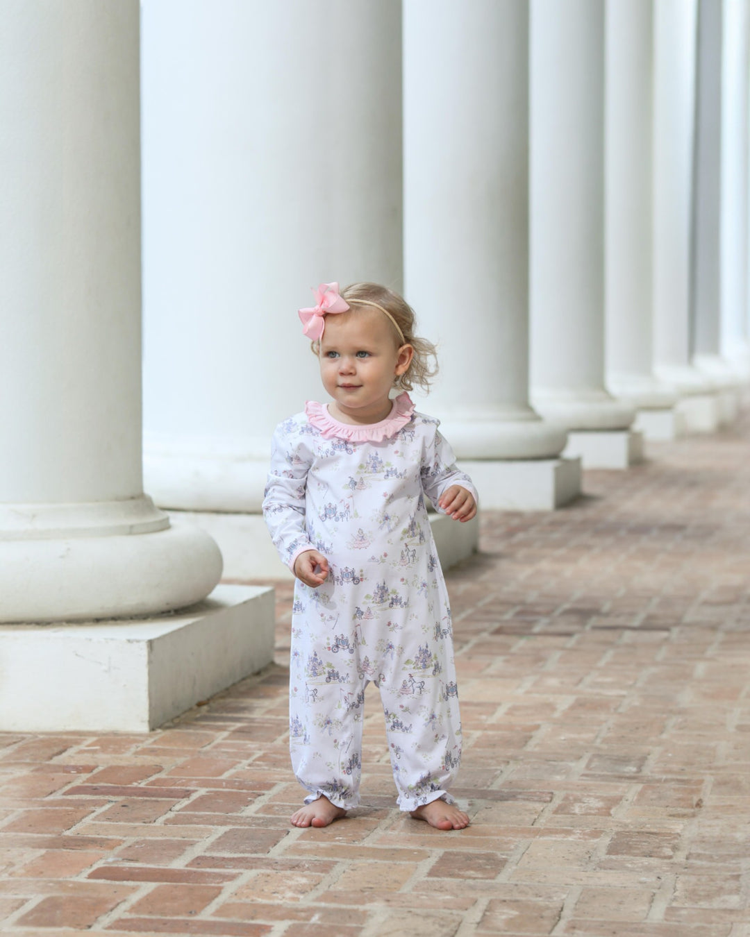 Young child in a floral outfit standing in front of classical columns.