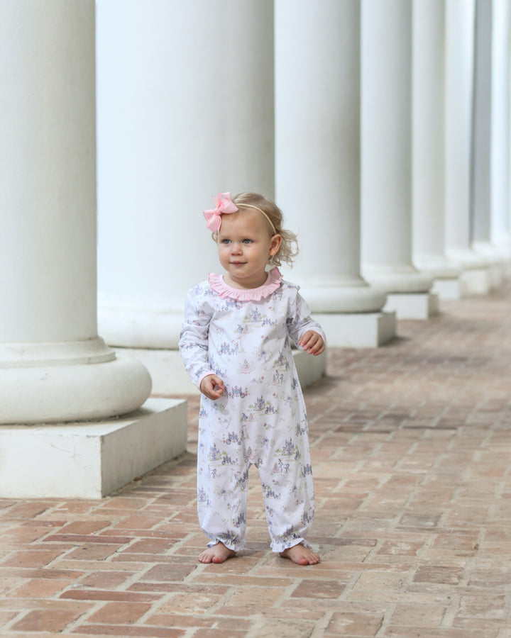 Young child in a floral outfit standing in front of classical columns.