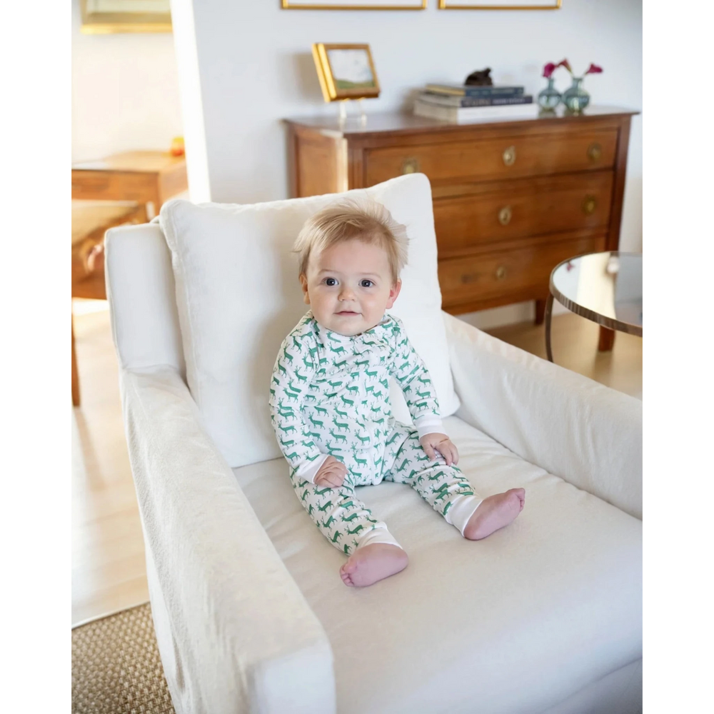 Baby in green and white pajamas sitting on a white chair in a room with wooden furniture.