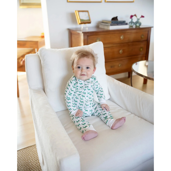 Baby in green and white pajamas sitting on a white chair in a room with wooden furniture.
