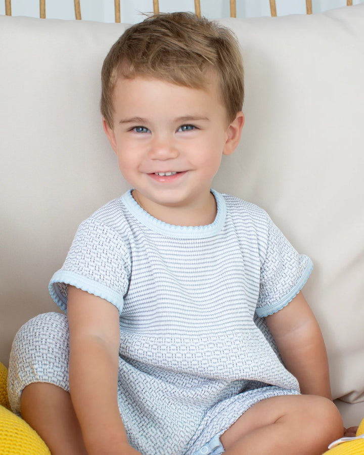 Child wearing a light blue and white textured outfit sitting on a beige couch.